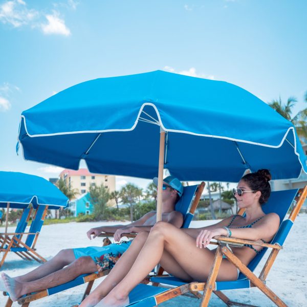 a group of people sitting at a beach with a umbrella in the sand