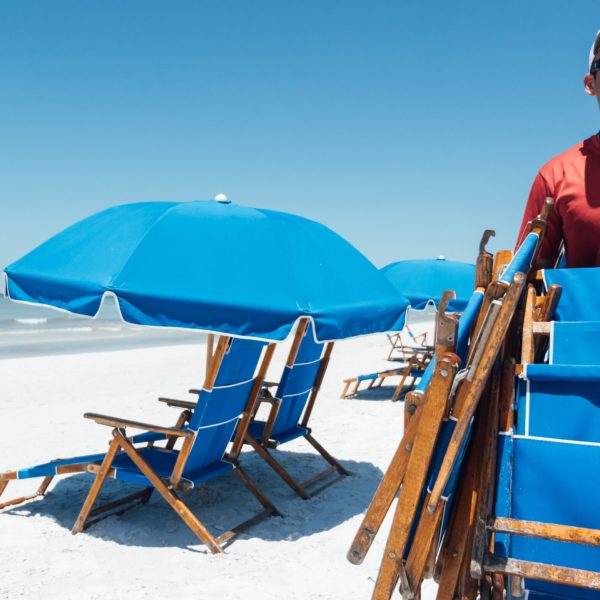 a person carrying chairs with a blue umbrella on the beach