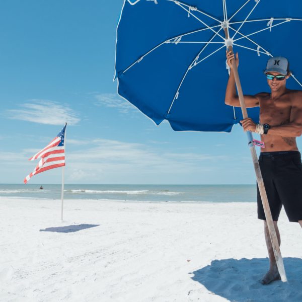 a person standing in front of a beach holding a blue umbrella