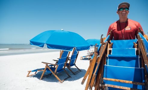 a person sitting in a chair with a blue umbrella on the beach