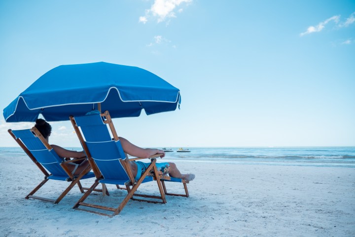 a couple of lawn chairs sitting on top of a sandy beach