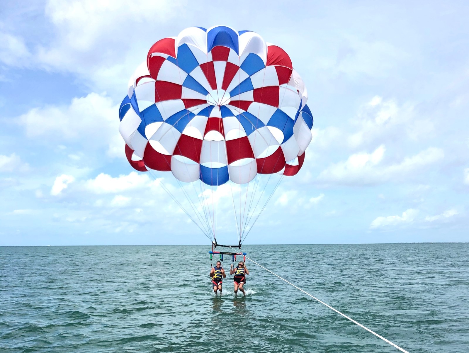 Two people parasailing over the ocean with a red, white, and blue parachute.